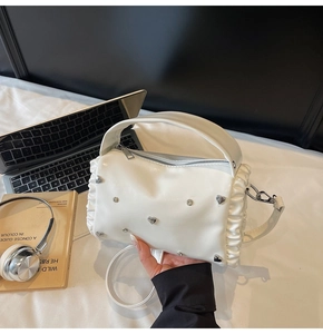 Detail of white leather tote with ruffled edges and silver heart studs on a desk