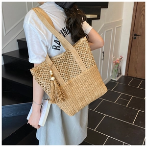 Detail of woven straw tote bag featuring intricate hollow mesh and tassel with wooden beads