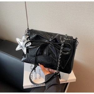 Detail of glossy black bow bag with silver chain strap and star charm accessory
