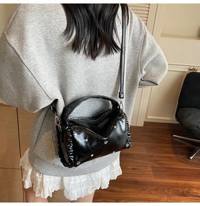 Detail view of black glossy tote bag with metal heart studs and side ruffles on shoulder strap