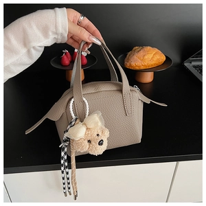 Détail d'un sac à main gris en cuir grainé avec breloque ours et ruban décoratif