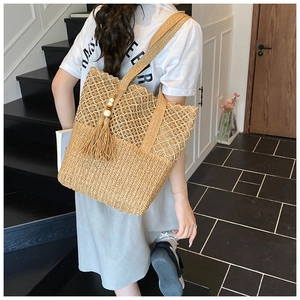 Detail of hollow woven straw shoulder bag with wooden bead tassel and textured mesh
