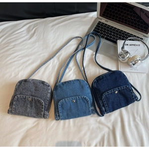 Three denim crossbody bags in grey, light blue and dark blue on a desk with a laptop