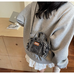 Detail of vintage gray denim mini crossbody bag featuring orange leather patch and metal tag