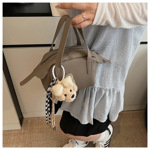 Détail d'un sac à main gris texture litchi avec un joli pendentif ours en peluche