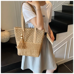 Detail of hollow-out straw tote bag with wooden bead tassel shown on female model
