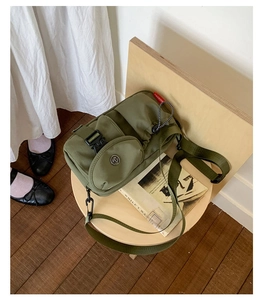Olive green nylon crossbody bag with multi-pocket design on a rustic wooden stool