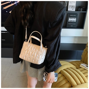 Detail of beige quilted bucket bag with rhinestone accents and dual carrying straps
