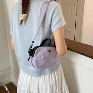 Detail view of purple nylon crossbody bag worn on shoulder to show size and fit