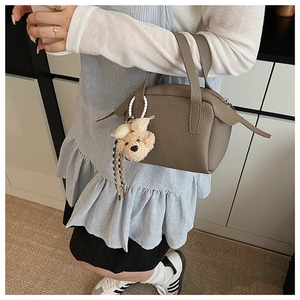 Détail d'un mini sac Boston en cuir taupe avec un adorable porte-clé ours en peluche