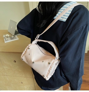 Detail of pink tote bag featuring heart rivets and ruffled trim on a wooden desk