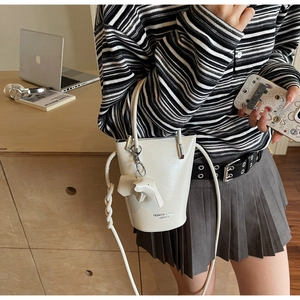 Detailed side view of a cream leather bucket bag with an elephant charm and woven strap
