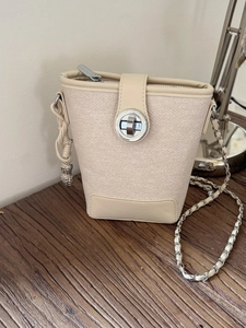 Cream bucket bag in canvas and leather with chain strap and peanut charm on wood surface