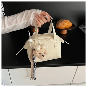 Détail d'un mini sac à main en cuir crème avec un charmant pendentif en peluche caniche