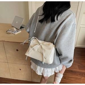 Détail d'un sac bandoulière blanc crème avec nœud décoratif et chaîne en métal élégante