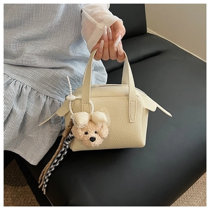 Détail du sac à main en cuir crème avec breloque ours et foulard élégant à pied-de-poule