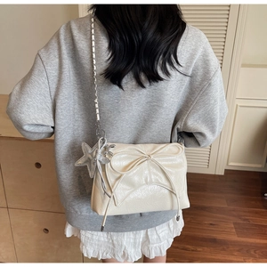 Détail du sac en cuir crème avec nœud et pendentif étoile sur chaîne argentée
