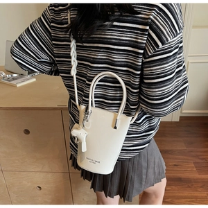 Detail of white bucket bag featuring elegant top handles and a cute bear bag charm