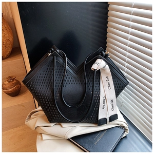 Détail d'un sac cabas noir ajouré au laser avec foulard décoratif sur un blazer