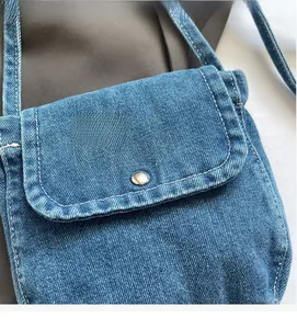 Detail of blue denim messenger bag showing metal button and white contrast stitching
