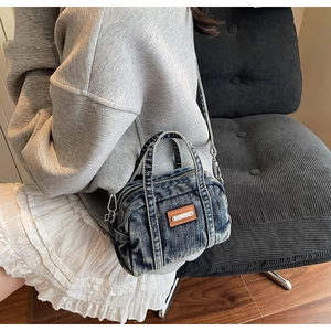 Close-up of a blue denim crossbody bag with brown leather patch on a model