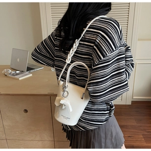 Detailed shot of cream leather bucket bag with braided strap and horse charm detail