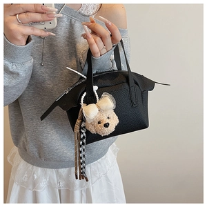 Détail d'un sac à main noir en cuir grainé avec un charmant ours en peluche et ruban