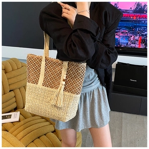 Detail of hollow woven straw tote bag featuring two-tone mesh design and tassel charm