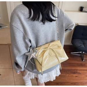 Détail du sac bandoulière crème avec nœud décoratif et pendentif étoile argenté brillant