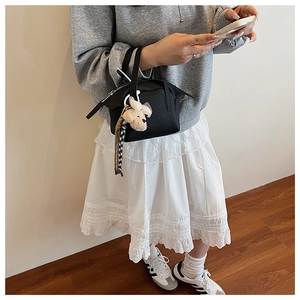 Détail d'un sac à main noir en cuir grainé avec charm chien en peluche et ruban