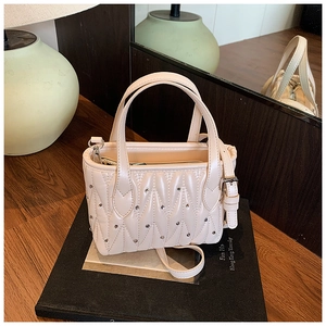Close-up of beige quilted leather bucket bag with silver studs and adjustable shoulder strap