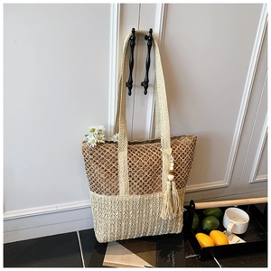Straw tote bag with hollow mesh design and fringe tassel against a white door background