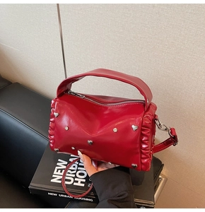 Detail of red cylindrical tote bag with silver heart studs and ruffles on a sofa