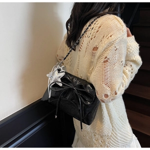 Détail du sac bandoulière en cuir verni noir brillant avec nœud et breloque étoile
