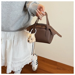 Détail d'un sac à main en cuir marron avec motif lychee et charmant ours en peluche