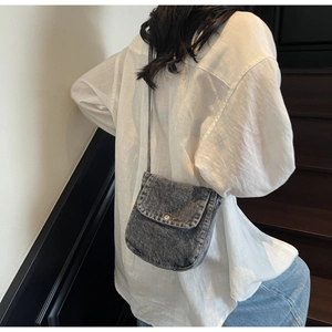 Detail of grey denim crossbody bag with metal buckle shown on a model's back