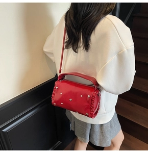 Detail view of red pleated crossbody bag featuring metallic heart studs and side ruffles