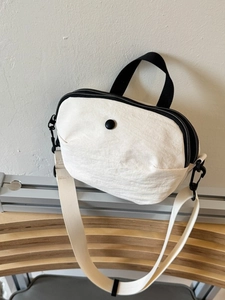Minimalist cream canvas crossbody bag with black handles and adjustable strap in soft light