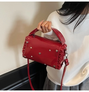 Close-up of red glossy patent leather tote bag with heart rivets and side pleated details