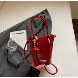 Close-up of red glossy patent leather bucket bag with silver zipper and leather charm