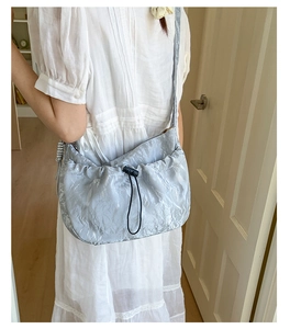 Model wearing a light blue pleated crossbody bag with metallic sheen and drawstring detail