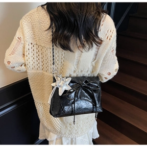 Détail du sac à bandoulière noir brillant avec nœud décoratif et pendentif étoile