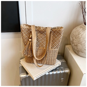 Detailed hollow-out pattern and wooden bead tassel on a woven straw handbag