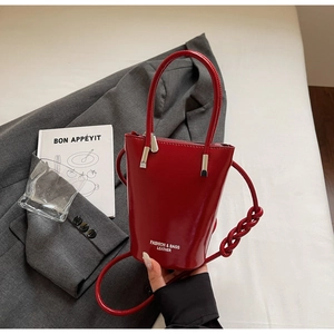 Detailed macro view of the red glossy leather bucket bag against a grey blazer jacket
