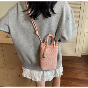 Détail d'un mini sac seau tressé rose avec bandoulière nouée et pendentif argenté