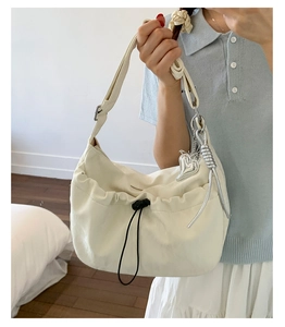 Detail of cream hobo bag with silver heart pendant and woven tassel shoulder strap