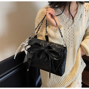 Détail du sac à bandoulière noir verni avec nœud, pendentif papillon et chaîne argent