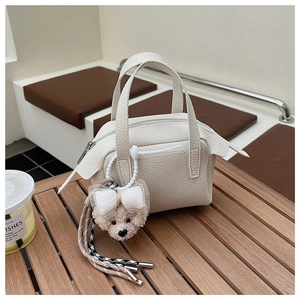 Détail d'un sac à main blanc grainé avec un charm ours en peluche sur une table en bois