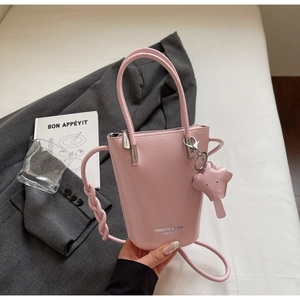 Detail of pink leather bucket bag featuring a woven strap and elephant charm accessory