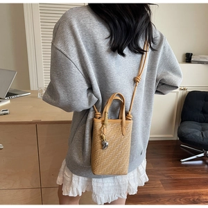 Détail d'un petit sac seau tressé beige avec breloque argentée et fine bandoulière